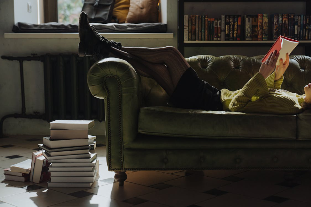 A person lying, reading on the couch with a pile of horror fiction